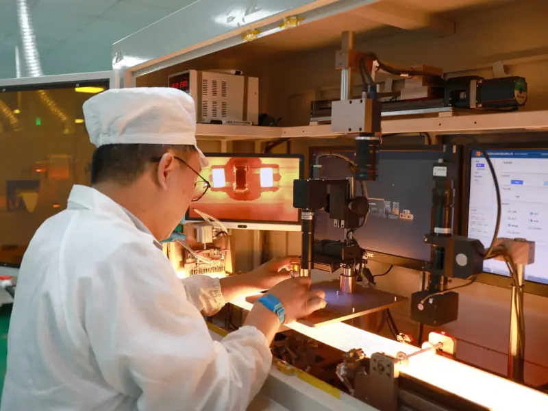 Technician at an automated lit-test station, machine-vision camera inspecting an illuminated LED strip on the conveyor