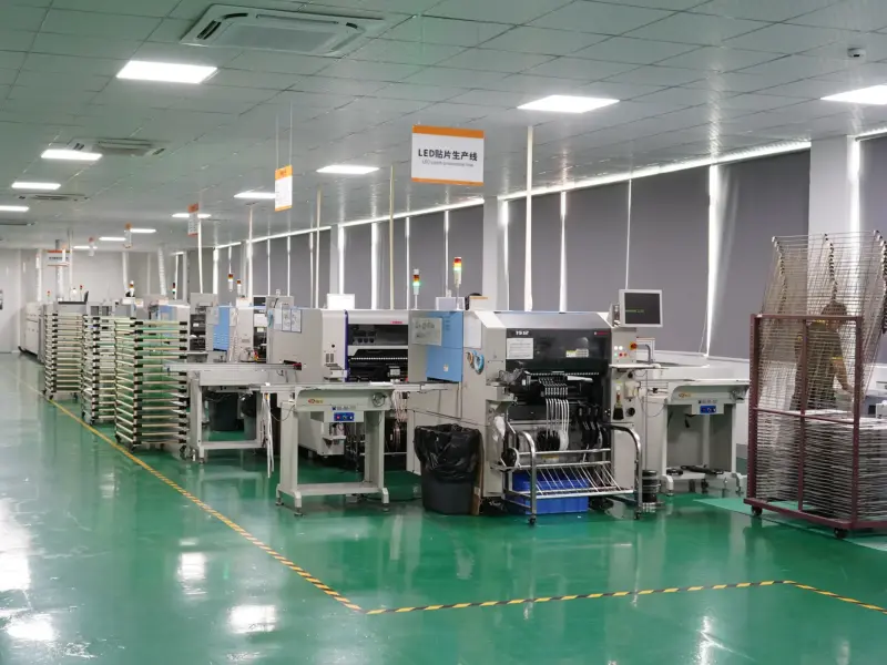 SMT pick-and-place line for flexible LED strip, with reflow oven and component feeder carts along a green epoxy floor