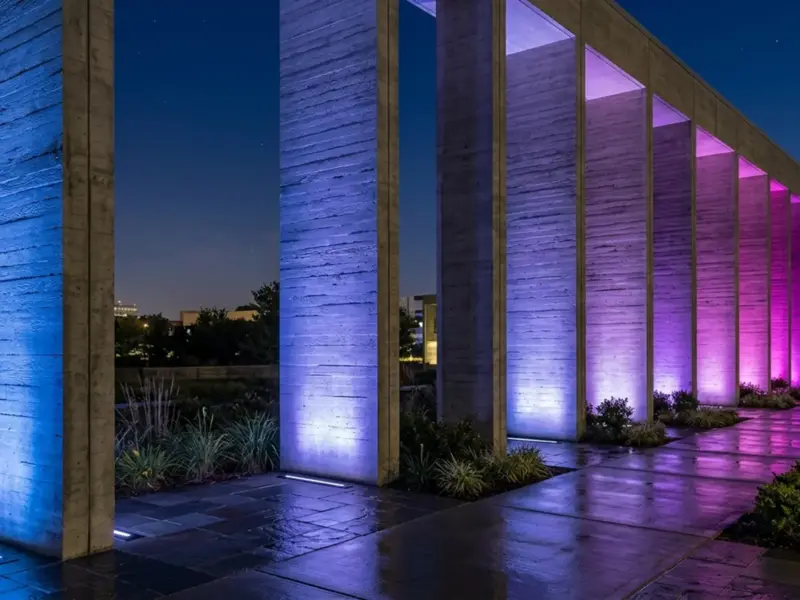 Concrete colonnade grazed from in-ground linear LED fixtures, each column holding a different color from blue to magenta