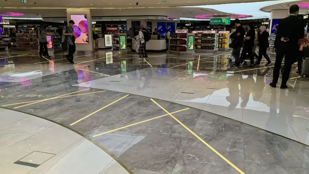 Warm 2700K in-ground linear light lines following a curved marble walkway in the Doha International Airport shopping area