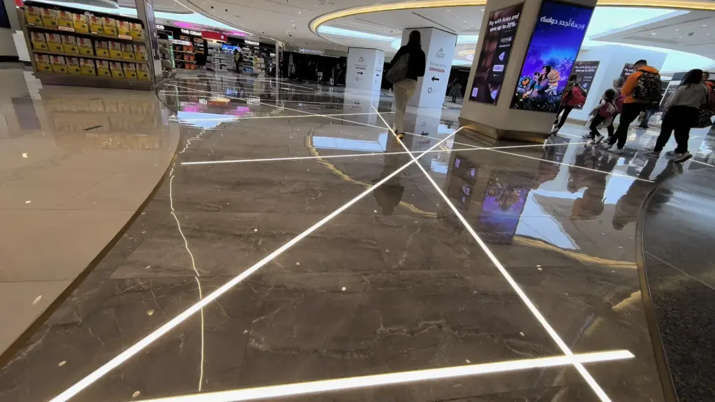 Cool 6000K in-ground linear light lines crossing the stone floor between shops at Doha International Airport