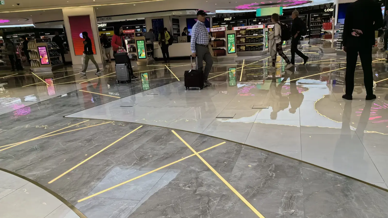 LED in-ground linear lights set flush in the stone floor of the Doha International Airport shopping area, with travelers pulling luggage over them