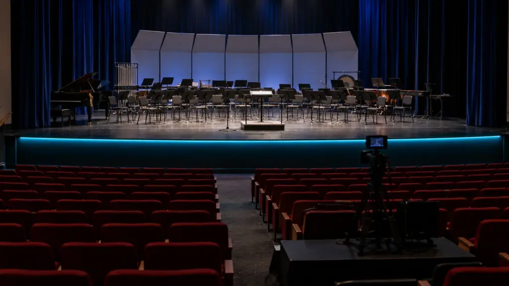 High school auditorium stage edge lined with black PCB addressable LED strip glowing cyan while the house is dark